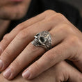 Load image into Gallery viewer, Oxidized filigree skull ring worn on a finger, close-up lifestyle shot showing deep shadows in the eye sockets and engraved scrollwork sides