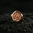 Load image into Gallery viewer, Rose gold plated raven signet ring with ornate emblem engraving and vintage-style relief, macro product shot on volcanic rock surface