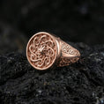 Load image into Gallery viewer, Rose gold plated round spiral signet ring with ornate swirling face design and patterned side panels, macro image on volcanic rock