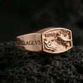 Load image into Gallery viewer, Rose gold plated Saint Michael ring with engraved lettering and sculpted battle tableau on the face, close-up photo on volcanic rock