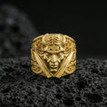 Load image into Gallery viewer, Gold plated devil head ring with crossed swords motif and detailed ornamental scrollwork, product-only macro image on black volcanic rock