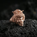 Load image into Gallery viewer, Rose gold plated geisha skull ring with ornate hair bun, flower accents, and carved skull-mouth detail, close-up product shot on volcanic rock