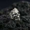 Load image into Gallery viewer, Polished silver skull ring featuring a wood bark texture finish and engraved side panels, close-up on volcanic stone