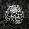 Load image into Gallery viewer, Oxidized sterling silver smoke skull ring with swirling flame-like curls and spiral eyes, macro photo on black volcanic rock