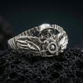 Load image into Gallery viewer, Polished silver motorcycle skull ring featuring sculpted wings and mechanical handlebar design, close-up on volcanic stone