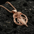 Load image into Gallery viewer, Rose gold plated raven and spear pendant on volcanic rock, textured lava stone background, high-relief metalwork detail