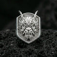 Load image into Gallery viewer, Polished silver Japanese oni mask ring with sharp horns and ornate swirl detailing, close-up on dark volcanic stone background