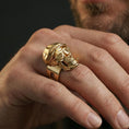 Load image into Gallery viewer, Gold plated finish skull ring worn on a finger, close-up lifestyle image focusing on the bold skull face and engraved depth