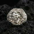 Load image into Gallery viewer, Sterling silver skull ring in a polished silver finish, high-relief eagle head and wing engraving with textured background, close-up on volcanic stone