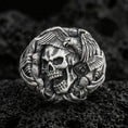 Load image into Gallery viewer, Sterling silver skull ring with an oxidized finish, eagle wings and claw details wrapping the band, macro on black volcanic rock