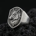Load image into Gallery viewer, Oxidized sterling silver wolf signet ring on textured volcanic rock, close-up macro showing detailed fur engraving and shield-shaped face