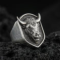 Load image into Gallery viewer, Oxidized sterling silver bull signet ring on textured volcanic rock, close-up macro showing horned head relief and shield-shaped face