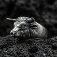 Load image into Gallery viewer, Oxidized sterling silver bull head ring on textured volcanic rock, macro close-up showing horns and nose ring detail in dark studio lighting