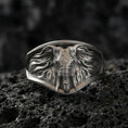 Load image into Gallery viewer, Oxidized sterling silver elephant signet ring on textured volcanic rock, macro close-up showing frontal elephant face, tusks, and flowing ear details