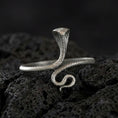 Load image into Gallery viewer, Oxidized sterling silver cobra snake ring on textured volcanic rock, macro close-up showing raised hood, coiled body, and detailed scale pattern