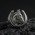 Load image into Gallery viewer, Oxidized sterling silver horseshoe horse ring on textured volcanic rock, macro close-up showing bridled horse head framed by a horseshoe design