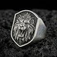 Load image into Gallery viewer, Close-up of an oxidized sterling silver roaring lion signet ring on porous volcanic rock in a dark studio setting