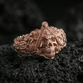Load image into Gallery viewer, Sterling silver Masonic skull ring with a rose gold plated finish, ornate gothic skull statement ring with symbolic eye triangle and scrollwork details, close-up on volcanic rock