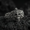 Load image into Gallery viewer, Sterling silver Masonic skull ring with an oxidized finish, all-seeing eye triangle and detailed floral carvings, macro on black volcanic rock