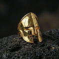 Load image into Gallery viewer, Sterling silver ancient Greek Spartan helmet ring with a gold plated finish, detailed warrior helm signet design with battle-worn texture, macro product shot on volcanic rock