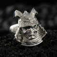 Load image into Gallery viewer, Sterling silver Japanese warrior helmet statement ring in a polished silver finish, sculpted samurai menpo mask design with ornate armor textures, close-up on volcanic stone