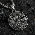 Load image into Gallery viewer, Sterling silver dragon medallion pendant with an oxidized finish, detailed coiled dragon relief with flowing clouds, close-up on black volcanic rock