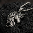 Load image into Gallery viewer, Oxidized unicorn head pendant necklace on textured volcanic rock, centered close-up highlighting the spiraled horn, flowing mane, and antique shadowed depth.