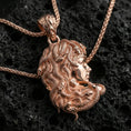 Load image into Gallery viewer, Rose gold plated Medusa profile pendant necklace on textured volcanic rock, centered studio-style close-up showcasing a soft rosy glow on the profile portrait and intertwined serpent detail.