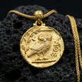 Load image into Gallery viewer, Gold plated owl coin pendant necklace on textured volcanic rock, premium close-up with warm reflective shine across the owl motif, laurel branch, and raised coin border.