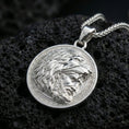 Load image into Gallery viewer, Polished silver Heracles lion helmet coin pendant necklace on textured volcanic rock, crisp macro product photo emphasizing clean edges, sharp sculpted beard detail, and bright reflective highlights.