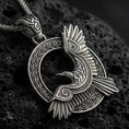 Load image into Gallery viewer, Oxidized Celtic raven knotwork pendant necklace on textured volcanic rock, centered close-up highlighting the winged raven silhouette, spiral accents, and deep antique contrast in the braided frame.
