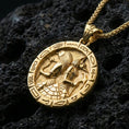 Load image into Gallery viewer, Gold plated Horus and Anubis pendant necklace on textured volcanic rock, premium close-up with warm reflective shine across the twin deity figures, staff-and-axe details, and raised symbol frame.