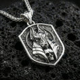 Load image into Gallery viewer, Polished silver Anubis pendant necklace on textured volcanic rock, crisp macro product photo emphasizing clean edges, sharp sculpted lines, and bright reflective highlights on the jackal mask relief.