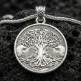 Load image into Gallery viewer, Polished silver Yggdrasil tree of life pendant necklace on textured volcanic rock, crisp macro product photo emphasizing clean edges, sharp knotwork engraving, and bright reflective highlights on the tree relief.