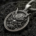 Load image into Gallery viewer, Oxidized demon mask medallion pendant necklace on textured volcanic rock, centered close-up highlighting the horned oni-style face, sharp fangs, and deep antique shadowed contrast.