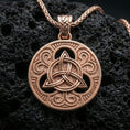 Load image into Gallery viewer, Rose gold plated Celtic triquetra pendant necklace on textured volcanic rock, centered studio-style close-up showcasing soft rosy glow and intricate Celtic scroll-and-knot detailing.
