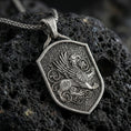 Load image into Gallery viewer, Oxidized griffin shield pendant necklace on textured volcanic rock, centered close-up highlighting the winged guardian gryphon, ornate scroll accents, and deep antique shadowed contrast.