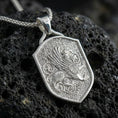 Load image into Gallery viewer, Polished silver griffin shield pendant necklace on textured volcanic rock, crisp macro product photo emphasizing clean edges, sharp feather lines, and bright reflective highlights on the raised relief.