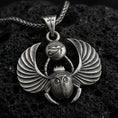 Load image into Gallery viewer, Oxidized winged scarab beetle pendant necklace on textured volcanic rock, centered close-up highlighting the spread wings, scarab body relief, Eye of Ra detail, and deep antique shadowed contrast.