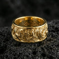 Load image into Gallery viewer, Gold plated koi fish band ring on textured volcanic rock, premium close-up with warm reflective shine across the koi motifs, swirling wave details, and raised ornamental contours.