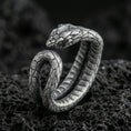 Load image into Gallery viewer, Oxidized snake wrap ring on textured volcanic rock, centered close-up highlighting the coiled body, scale texture, and deep antique shadowed contrast.