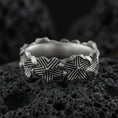 Load image into Gallery viewer, Oxidized floral band ring on textured volcanic rock, centered close-up highlighting the raised lily motifs, carved line texture, and deep antique shadowed contrast.