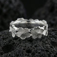 Load image into Gallery viewer, Polished silver floral band ring on textured volcanic rock, crisp macro product photo emphasizing clean edges, sharp flower relief, and bright reflective highlights across the patterned band.