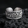 Load image into Gallery viewer, Oxidized skull cuff ring on textured volcanic rock, centered close-up highlighting the clustered skull texture, open band design, and deep antique shadowed contrast.
