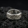 Load image into Gallery viewer, Polished silver Celtic triquetra band ring on textured volcanic rock, crisp macro product photo emphasizing clean edges, sharp knotwork relief, and bright reflective highlights across the band.
