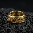 Load image into Gallery viewer, Gold plated Celtic triquetra band ring on textured volcanic rock, premium close-up with warm reflective shine across the repeating Trinity knots and raised contours.