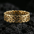 Load image into Gallery viewer, Gold plated Celtic triquetra chain-link ring on textured volcanic rock, premium close-up with warm reflective shine across the interlocking Trinity knot links and raised contours.