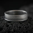 Load image into Gallery viewer, Oxidized diagonal groove band ring on textured volcanic rock, centered close-up highlighting the slanted line engraving and deep antique shadowed contrast across the channel pattern.