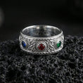 Load image into Gallery viewer, Polished silver ornate gemstone band ring on textured volcanic rock, crisp studio macro emphasizing the raised scrollwork, beaded borders, and three gemstone settings with bright reflective shine.