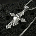 Load image into Gallery viewer, Polished silver praying hands cross pendant on porous volcanic stone, close-up highlighting the raised hand sculpture, crisp cross edges, and clean reflective finish